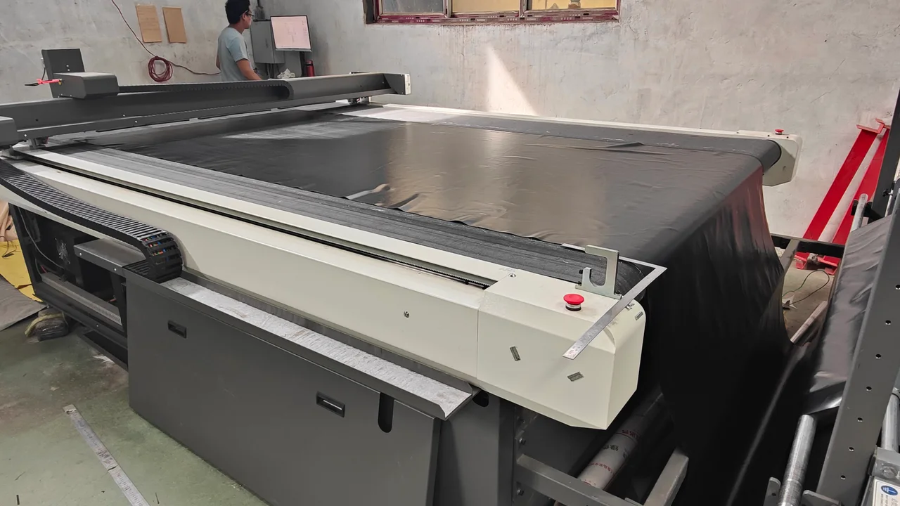 Large dark tent fabric panel laid across a digital cutting table in the factory