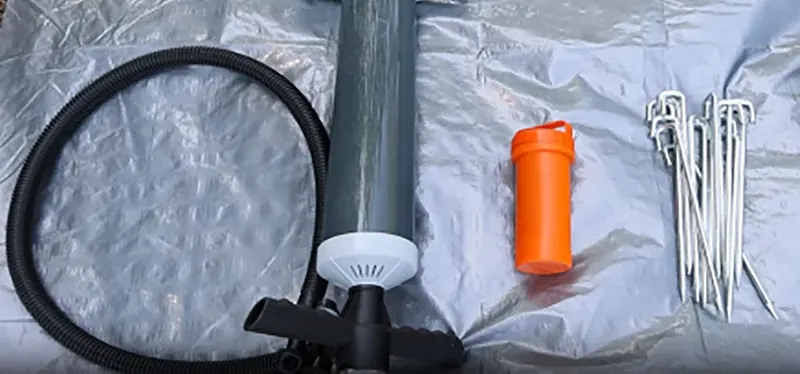 Hand pump with a black hose, an orange bottle and metal ground pegs laid out on grey fabric
