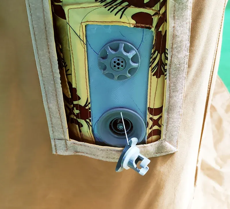 Close view of a tan shelter wall with a patterned lining panel holding an inflation valve and cap