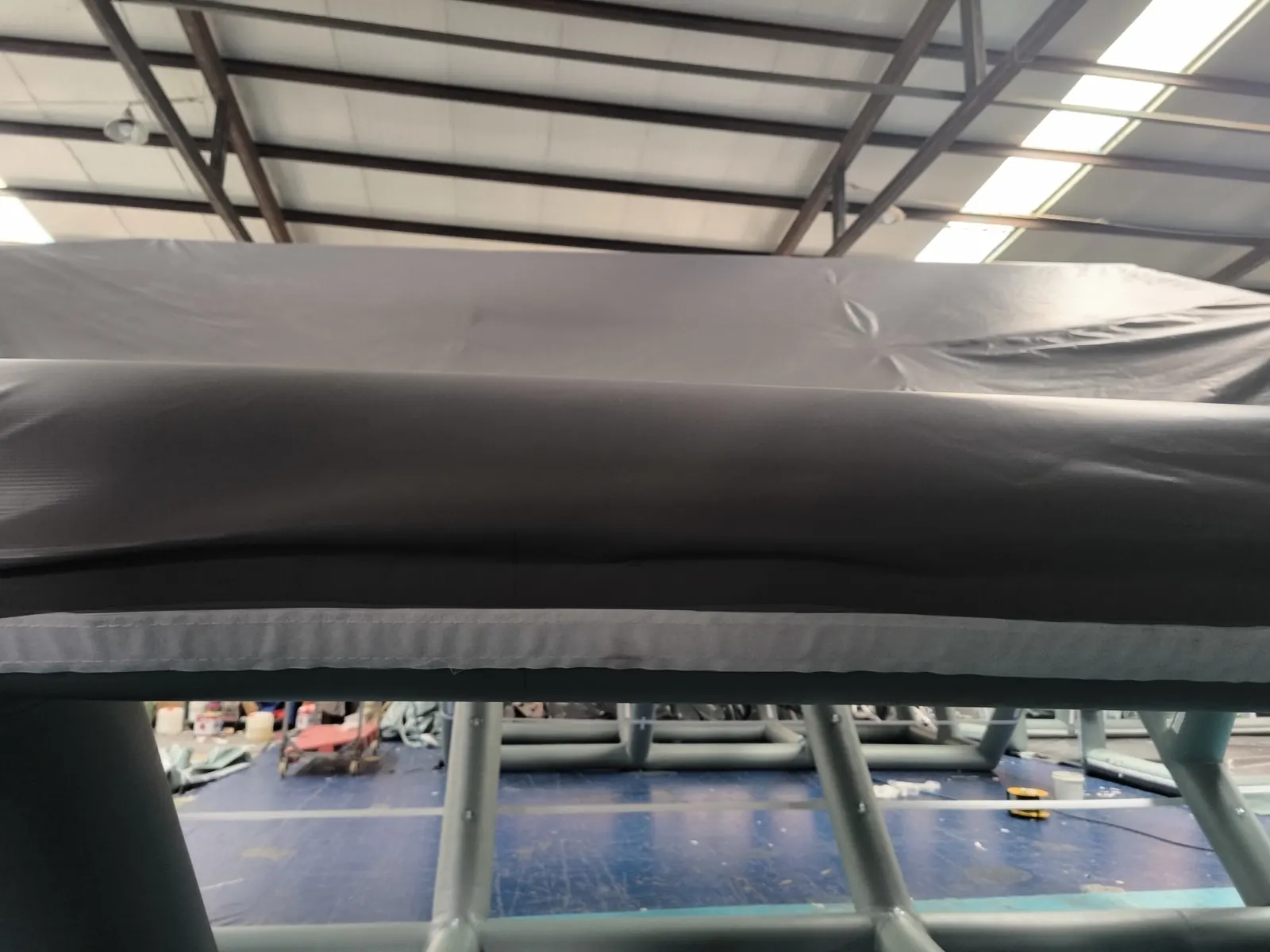 Close view of a dark air-beam top tube and fabric panel edge under a steel workshop roof