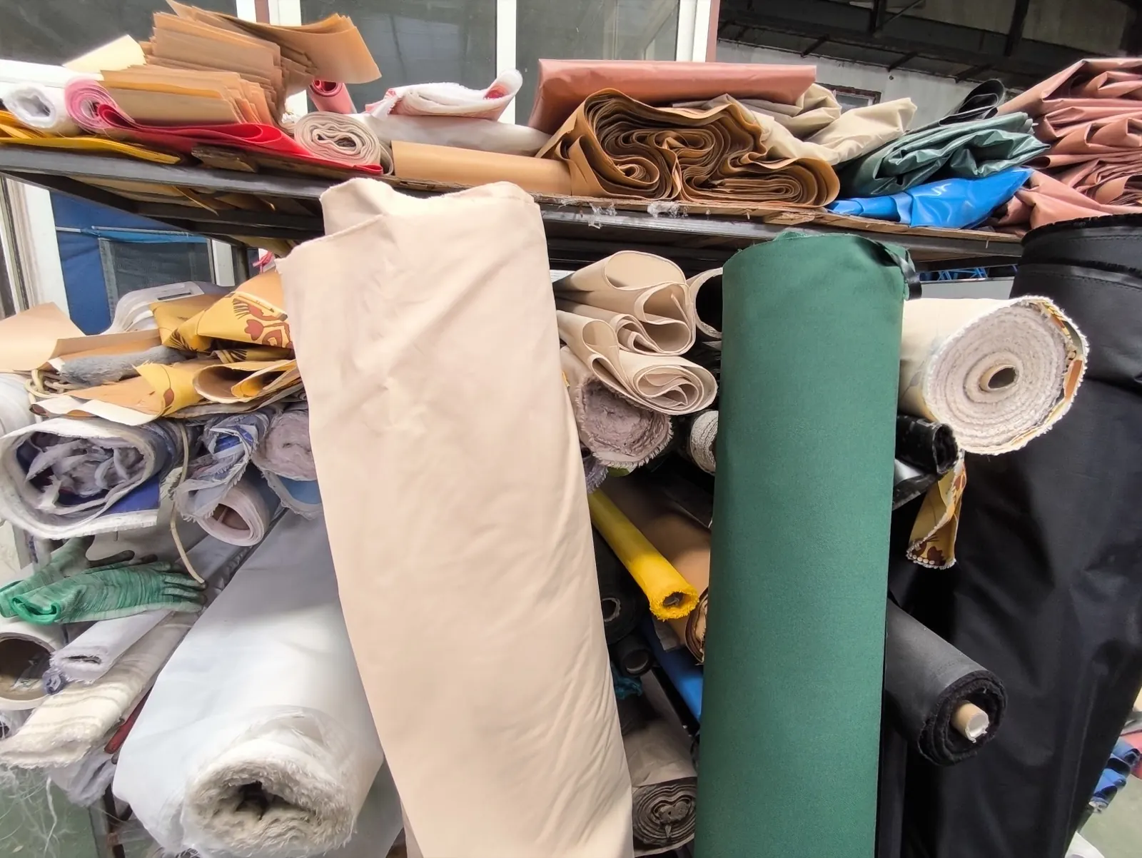 Shelves of coloured coated fabric rolls and folded fabric sections in a tent workshop