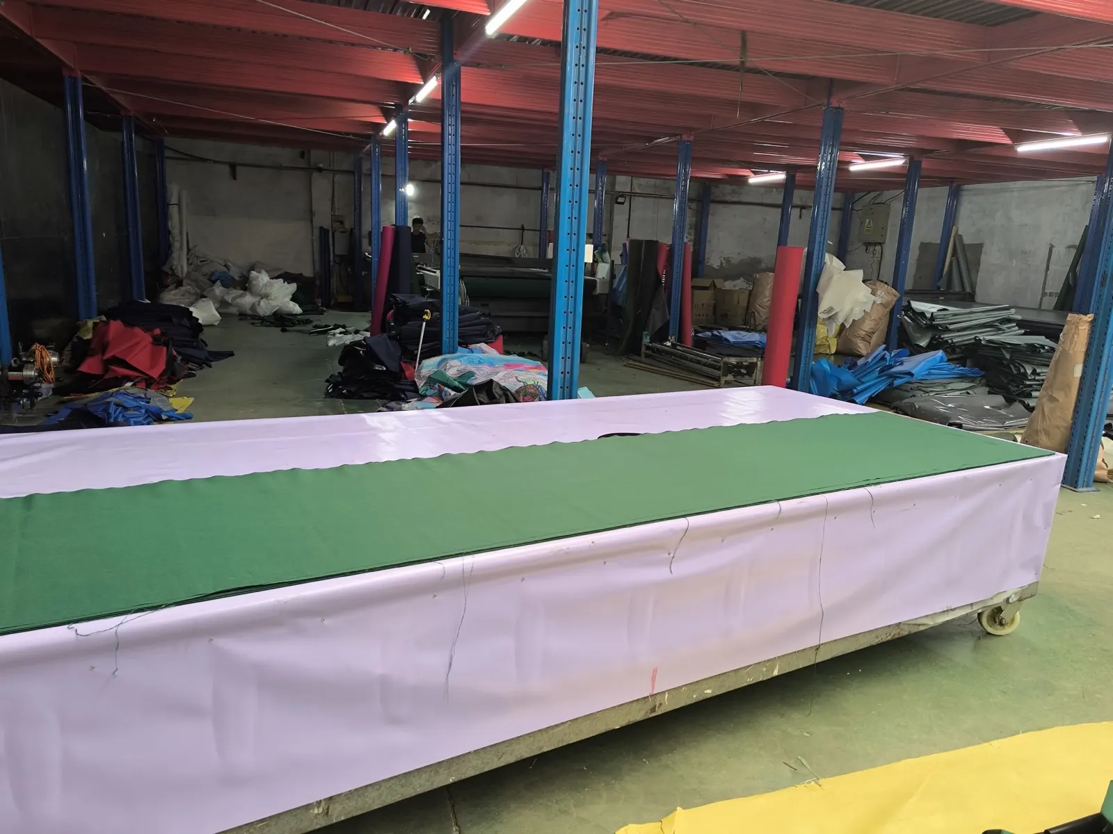 Green and white fabric layers laid along a wheeled cutting table in the production workshop