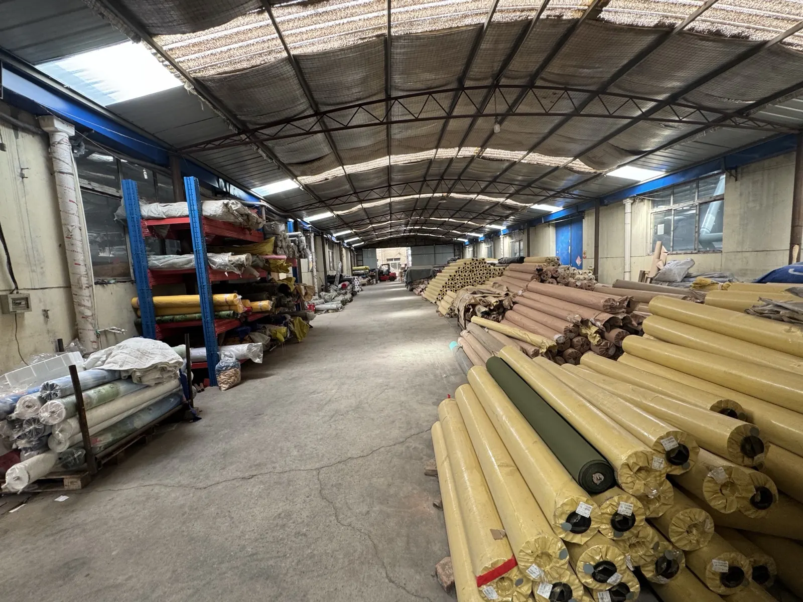 Wide warehouse aisle lined with stacked rolls of yellow and olive coated tent fabric and steel racking