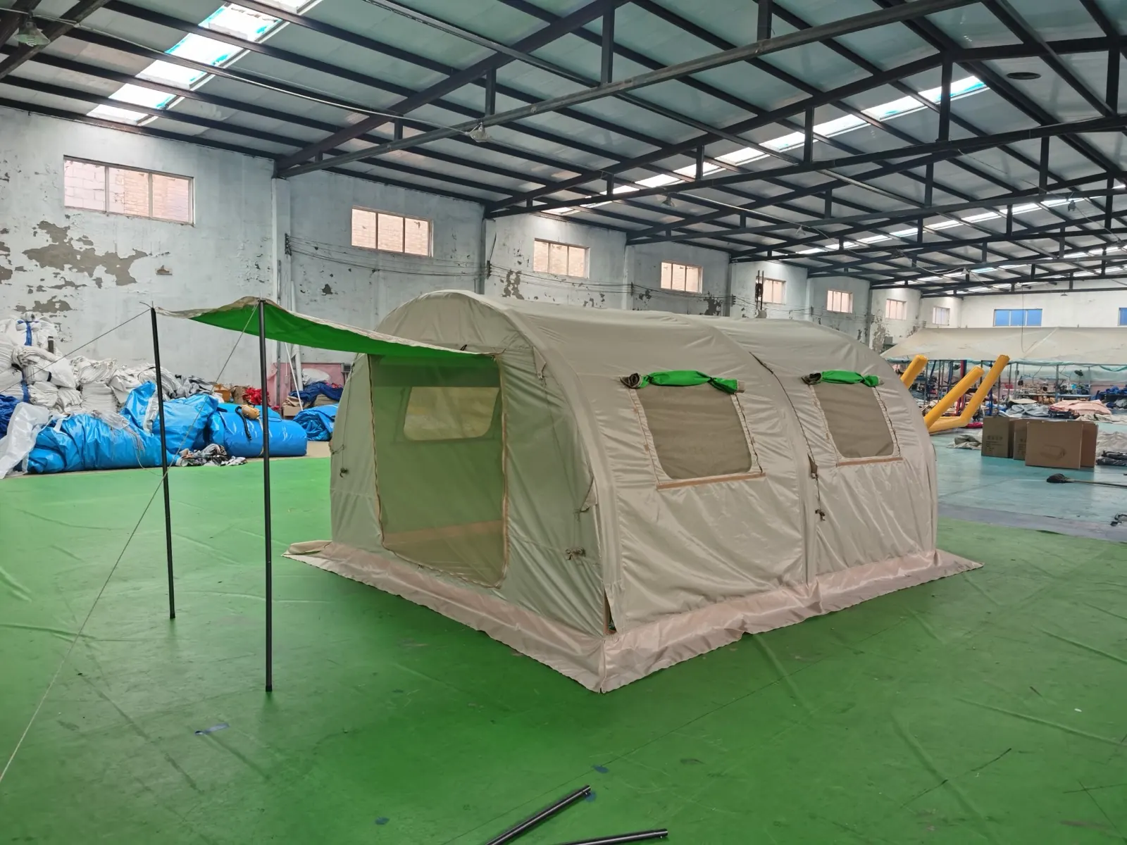 Beige air-beam shelter entrance side with awning poles and a visible ground layer