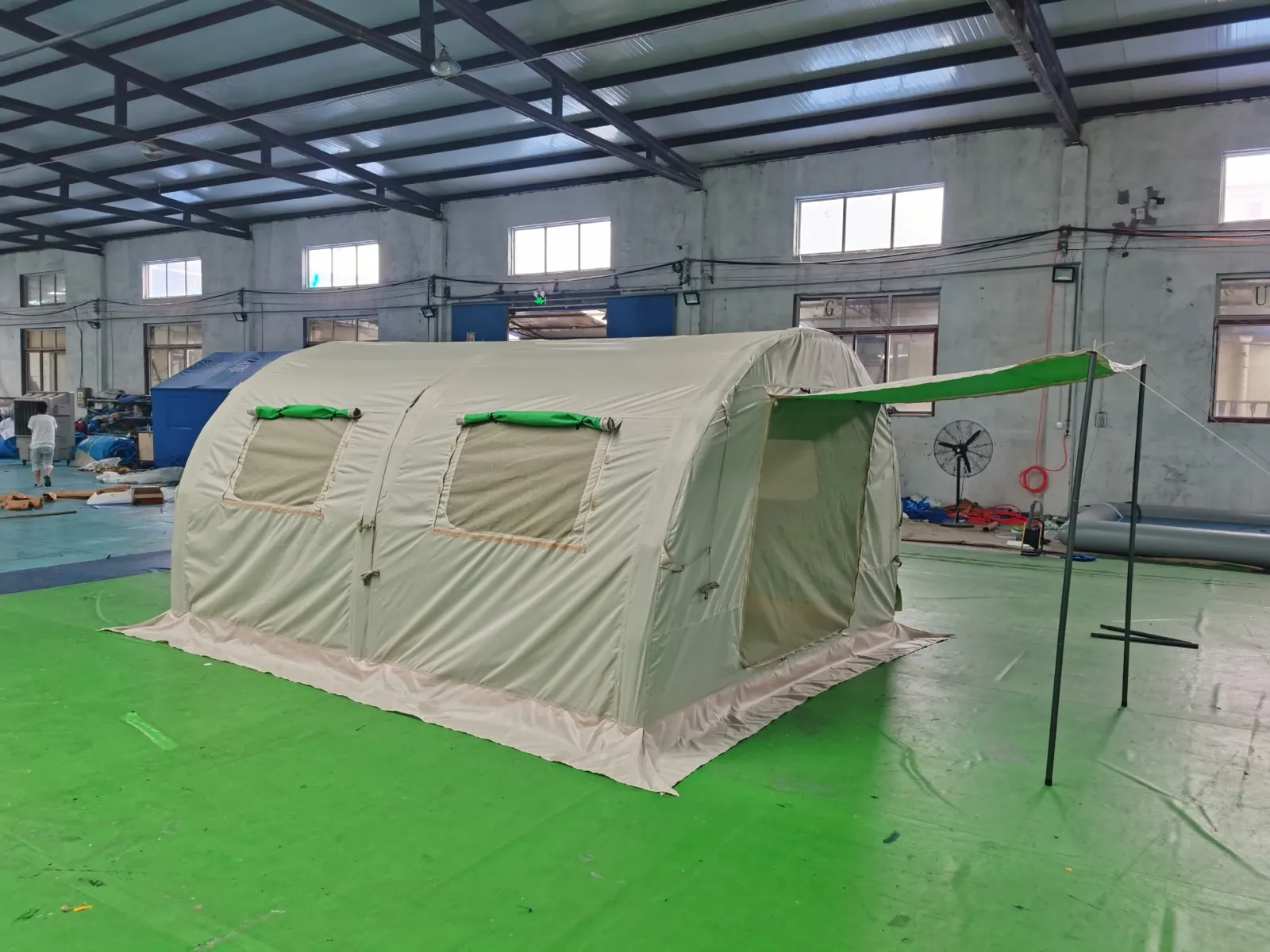 Beige air-beam shelter with two windows and a green entrance awning on a green workshop floor