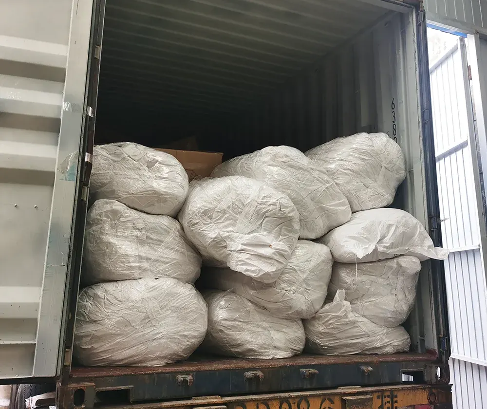 White woven bags of folded shelters stacked inside an open shipping container