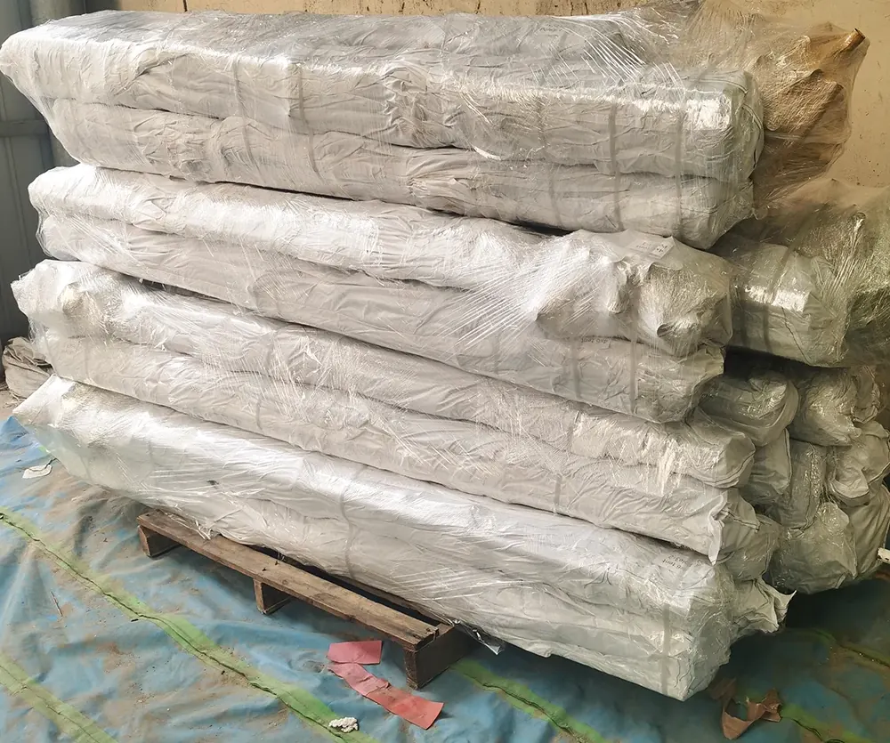 Stack of shrink-wrapped fabric bales on a wooden pallet on a blue sheet