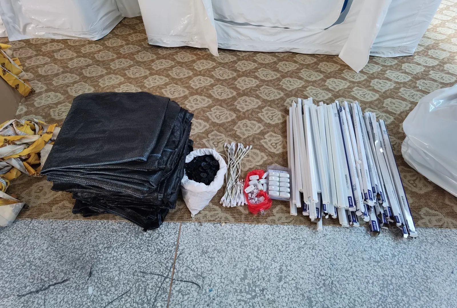 Poles, fabric bundles, cord and small fittings laid out on a carpeted floor