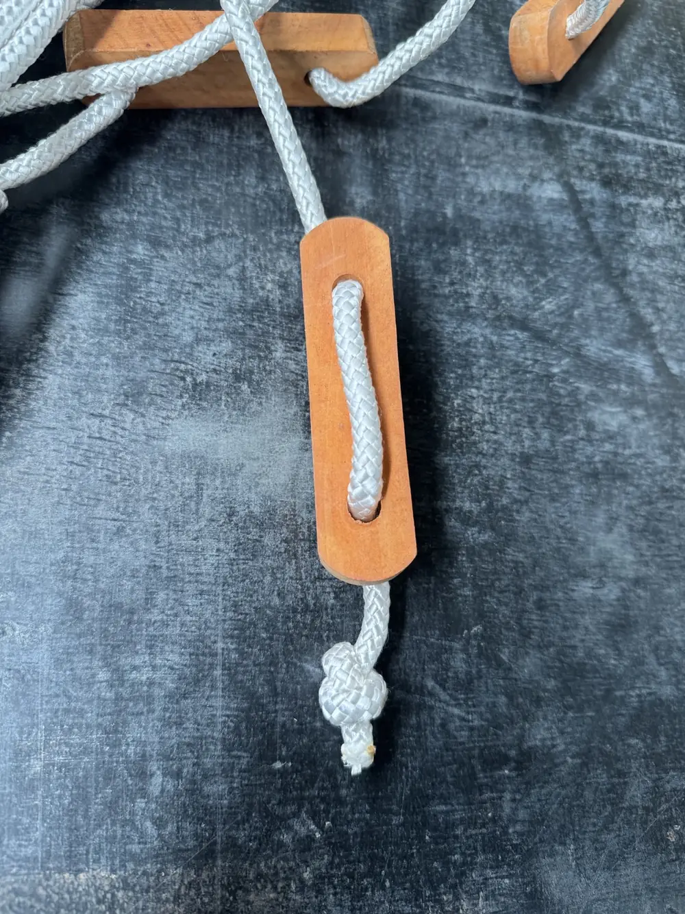 Wooden toggle with knotted white rope on dark coated fabric