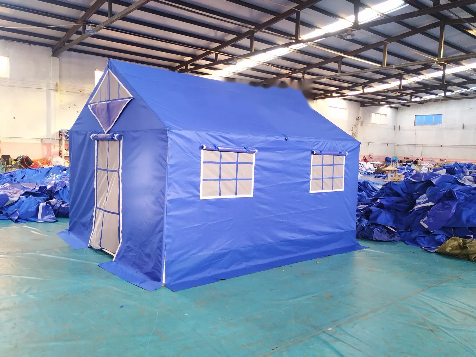Blue frame relief tent with a zipped door, gable window and two side windows in a workshop