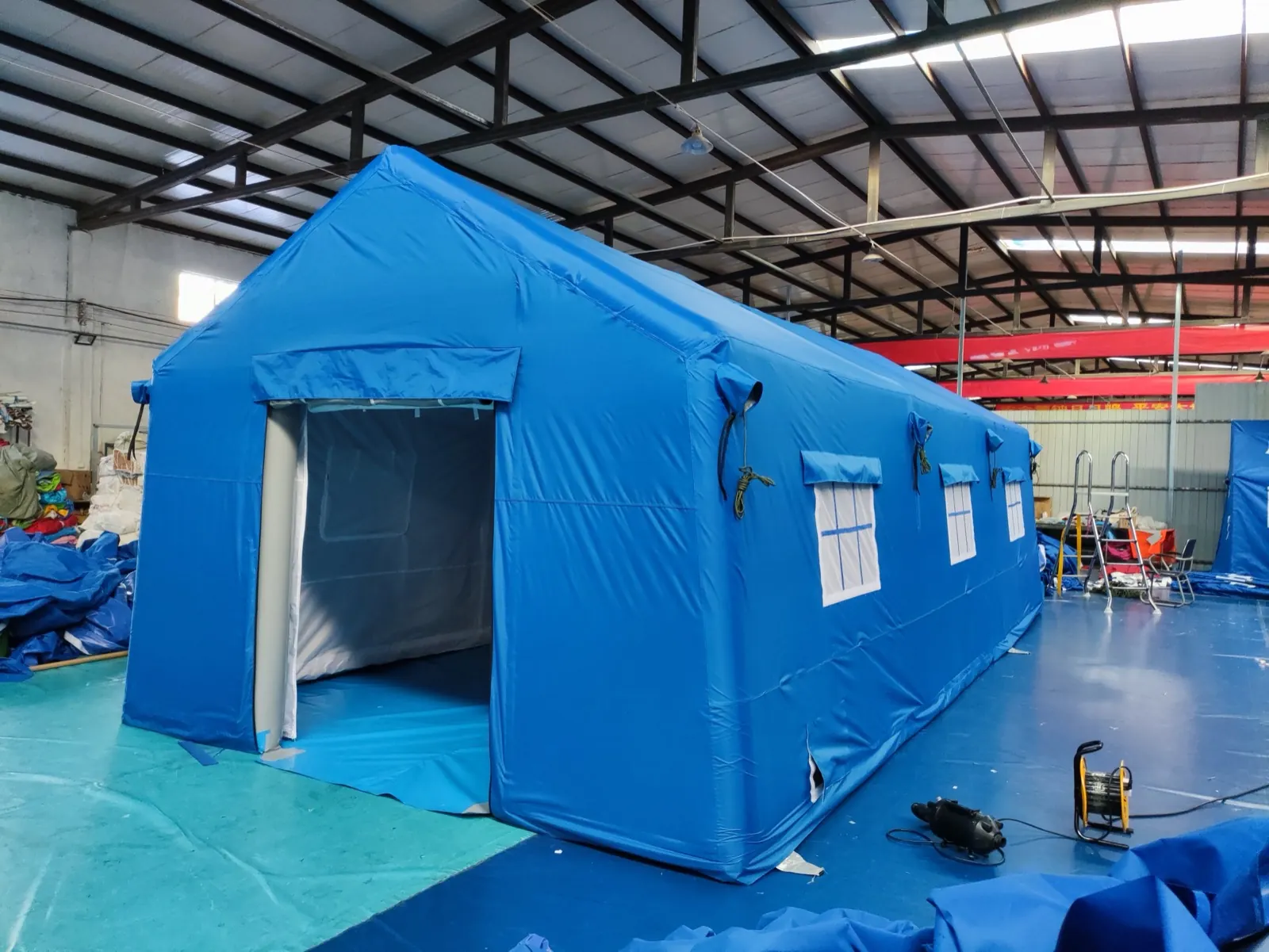 Large blue relief shelter with an open doorway and side windows in a workshop